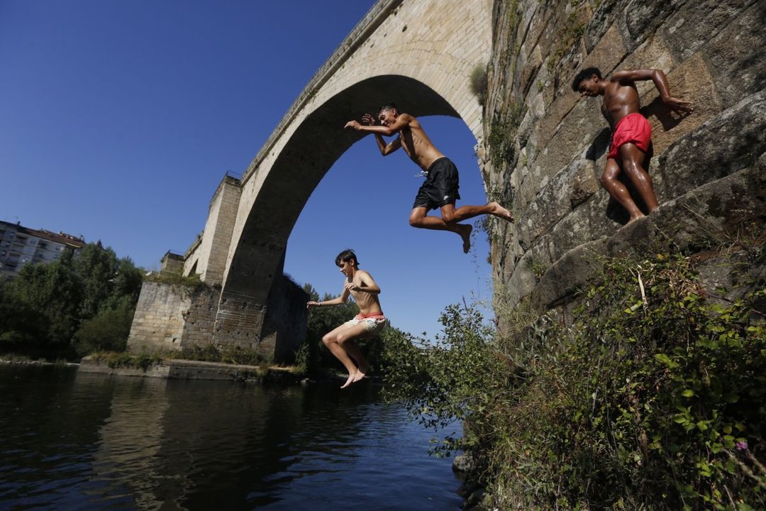 Tres jóvenes saltan al agua del Miño desde el Puente Romano (Foto: Marcos Atrio).