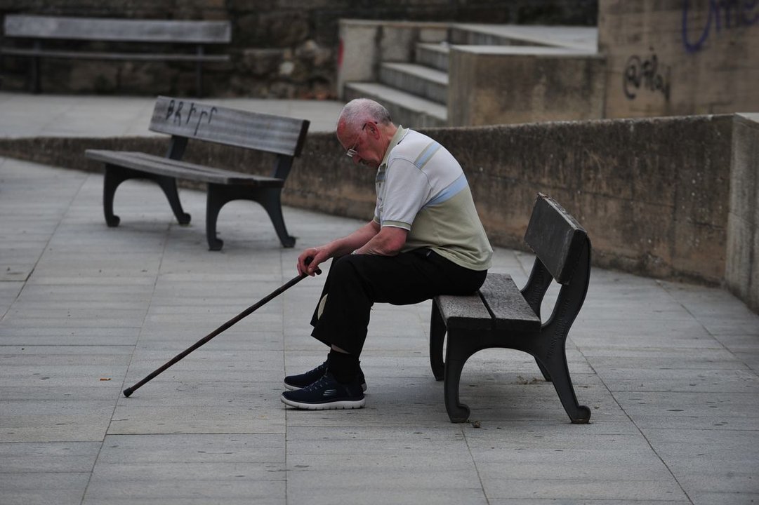 Una persona mayor descansa en un banco de la ciudad.