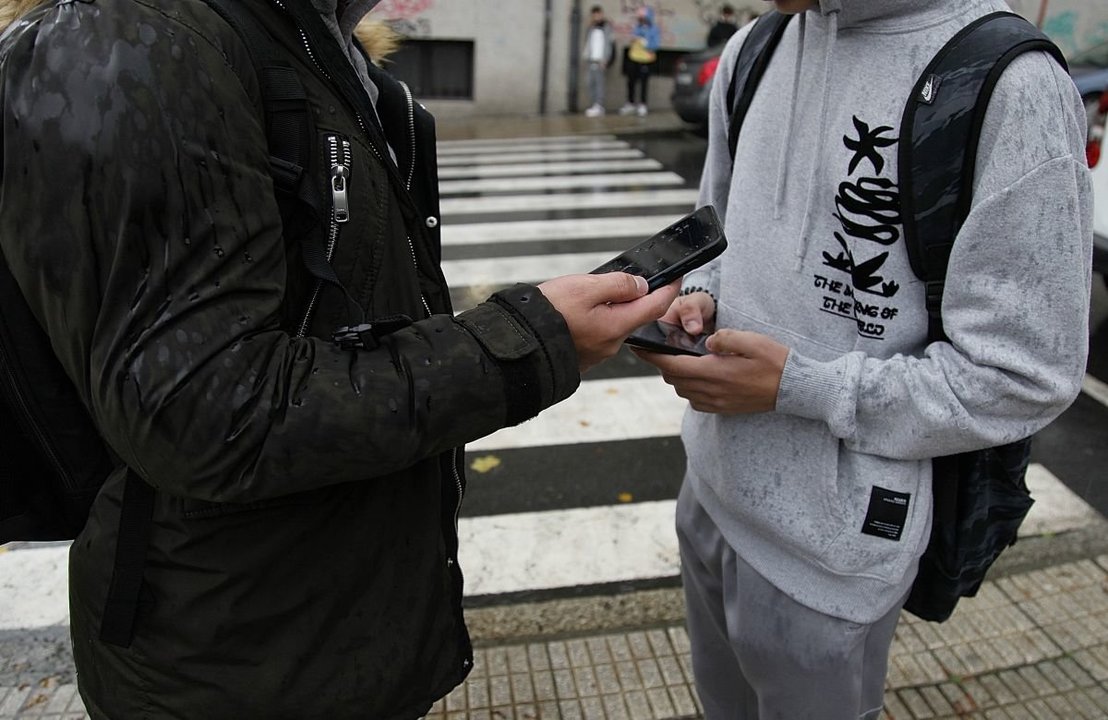 Dos adolescentes utilizan su dispositivo móvil a la salida del instituto, en Ourense.