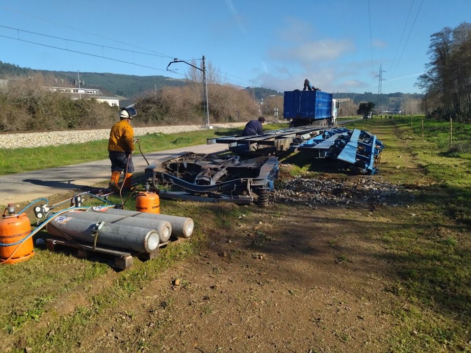 Dos operarios desmontan los restos de vagones descarrilados.